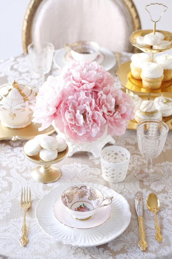 a refined vintage bridal shower tablescape with a lace tablecloth, pink peonies, neutral and blush porcelain and gold cutlery