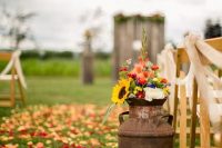 a rustic fall wedding aisle with colorful petals, a rusty churn with bold blooms and greenery is a cool and lovely idea
