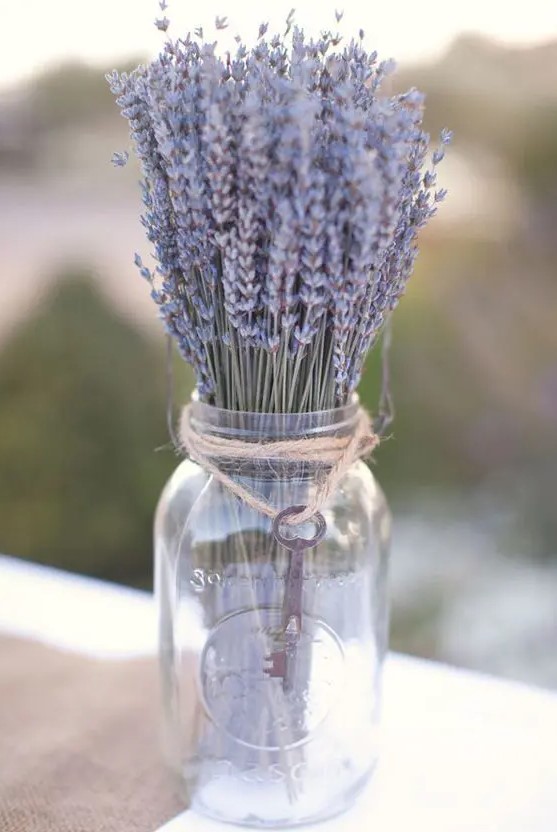 a rustic summer wedding centerpiece of a clear mason jar, lavender, twine and a vintage key is easy to make yourself