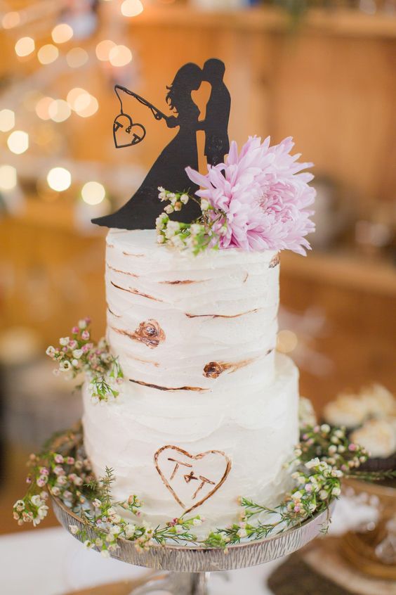 a rustic wedding cake imitating birch bark, with white blooms and greenery and a black silhouette cake topper is amazing