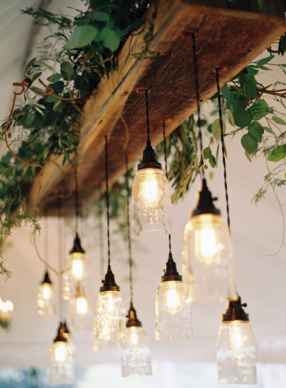 a rustic wedding chandelier of a wooden piece, greenery and twigs, pendant lamps made of mason jars is a cool idea