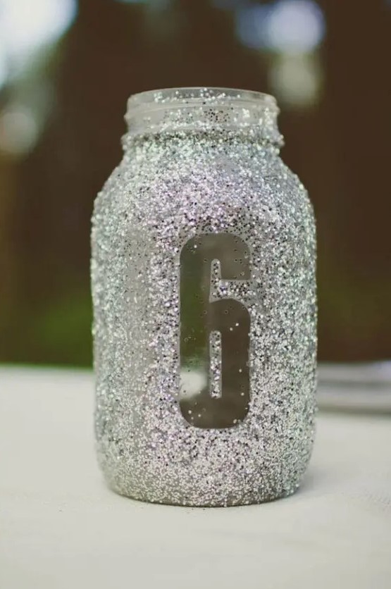 a silver glitter mason jar with a table number doubles as a candle lantern, perfect for a winter wedding with a ouch of sparkle
