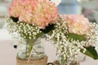a tree slice with mason jars wrapped with burlap and with pink hydrangeas and white baby’s breath, vine hearts for a rustic wedding
