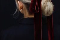 a twisted low bun with a volume on top accented with an oversized burgundy velvet ribbon bow for a bold look