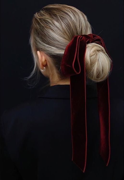 a twisted low bun with a volume on top accented with an oversized burgundy velvet ribbon bow for a bold look