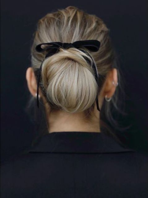 a twisted low updo with a large bun and a black velvet ribbon bow is a chic and refined idea for a wedding