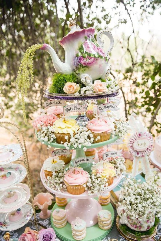 a vintage bridal shower dessert table with a cupcake stand with baby's breath and a teapot on top, with some vintage sweets stands