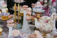 a vintage bridal shower dessert table with vintage teaware, cupcakes, donuts and other sweets, pink roses and vases