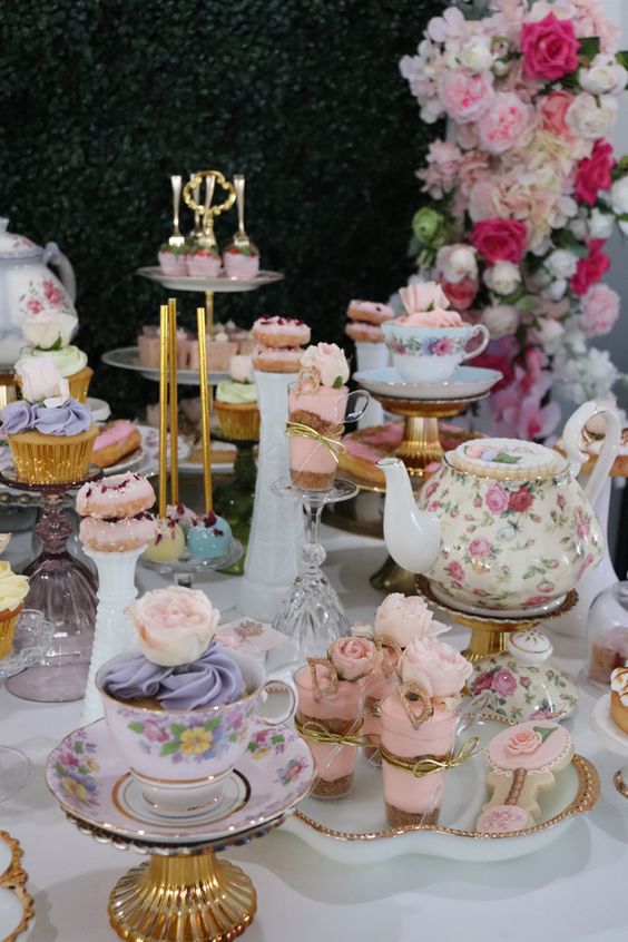 a vintage bridal shower dessert table with vintage teaware, cupcakes, donuts and other sweets, pink roses and vases