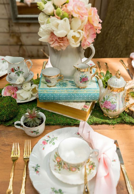 a vintage bridal shower tablescape with a greenery runner, potted succulents, pastel blooms, floral porcelain and gold cutlery