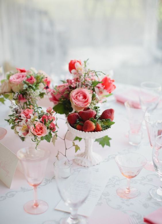 a vintage cluster wedding centerpiece of pink and white blooms and greenery and some strawberry in a bowl for a summer feel