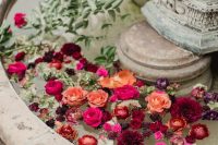 a vintage fountain styled with floating burgundy, orange, red and hot pink blooms and greenery for a lovely wedding