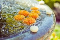 a vintage fountain with floating orange dahlias and candles is a very bright and easy outdoor decor idea