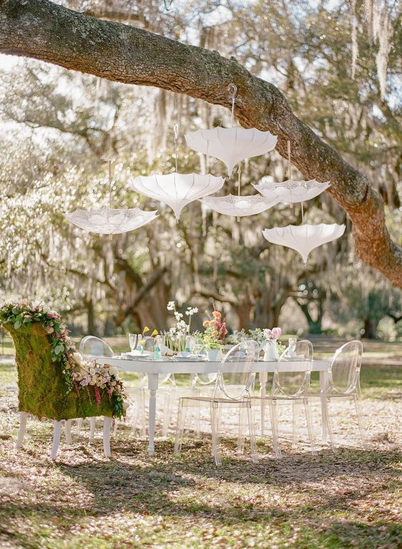 a vintage-inspired bridal shower tablescape with some pastel blooms, umbrellas over the table and a moss chair is a great idea
