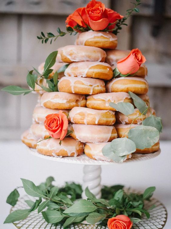 a vintage stand with glazed donuts, greenery and orange roses on top is a great idea for a vintage bridal shower