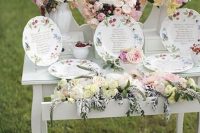 a vintage vanity with a mirror, pastel and neutral blooms and plates with painted blooms and a seating plan on them