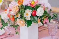 a wedding centerpiece of a white vase, lilac, pink and peachy blooms, greenery and strawberries is perfect for summer