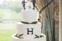 a white textural wedding cake with greenery, a monogram and black silhouette cake toppers plus a little dog figurine