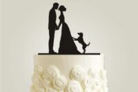 a white wedding cake with sugar blooms and a silhouette cake topper showing the couple and their dog is very cute