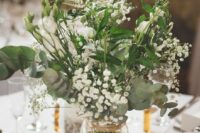 an airy barn wedding centerpiece of a wood slice, a wood slice table number and neutral blooms and greenery in a jar