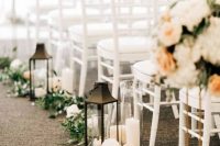 an elegant fall wedding aisle lined up with neutral blooms, greenery and candle lanterns plus lush neutral floral arrangements