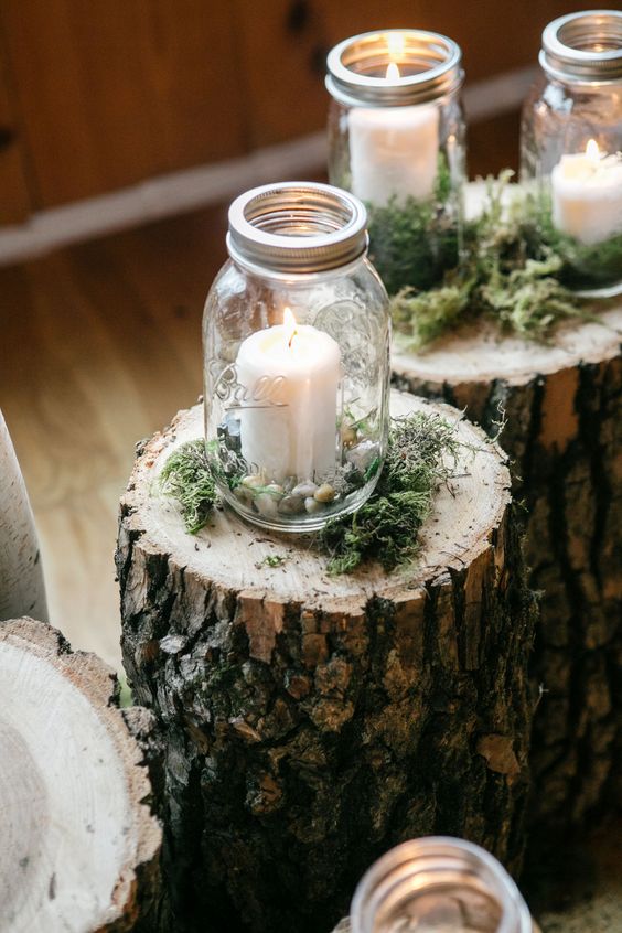 mason jar wedding decor with candles and pebbles, placed on tree stumps with moss is a great idea for a rustic wedding