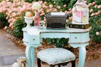 vintage bridal shower decor with a blue table and stool, a cage, some blooms and a typewriter plus vintage decor around