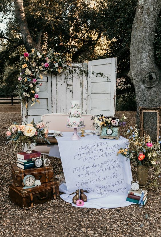 vintage bridal shower decor with vintage doors with blooms and greenery, stacked suitcases and books, clocks and a floral cake
