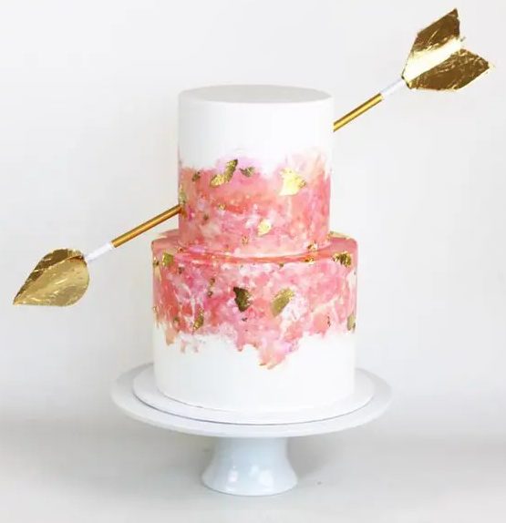 a Valentine wedding cake with pink and gold leaf decor, with an oversized gold arrow is bold and cool