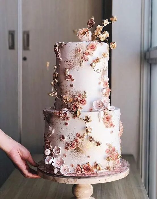 a beautiful blush wedding cake fully covered with pink and blush sugar blooms and gold blooming branches is wow