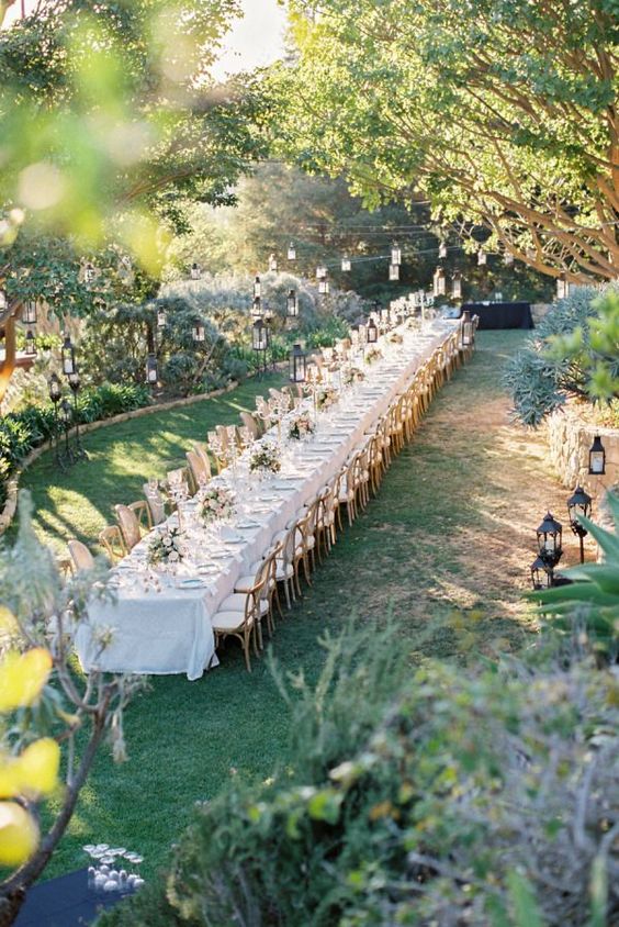 a beautiful vineyard wedding reception space with a long table done with neutral and pink blooms and jars with lights hanging over the space