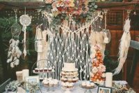 a boho dessert table with a macrame hanging, a doily tablecloth, some dreamcatchers, air plants and blooms