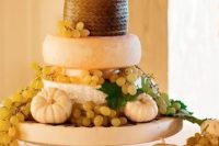 a bold and cool cheese wheel wedding cake with grapes, pumpkins and pretty doll-like toppers that look nice and cool