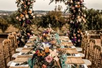 a bold vineyard wedding reception with bright florals and glasses, with an oversized lush floral arch is a cool idea