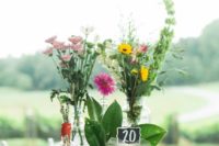 a bright summer wedding centerpiece of bottles and jars, bright wildflowers and greenery plus a table number