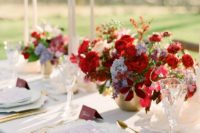 a bright vineyard wedding centerpiece of a gold vase with red and lilac blooms and some greenery