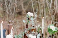 a catchy wedding centerpiece of apothecary bottles placed on stands and with white blooms and greenery in them