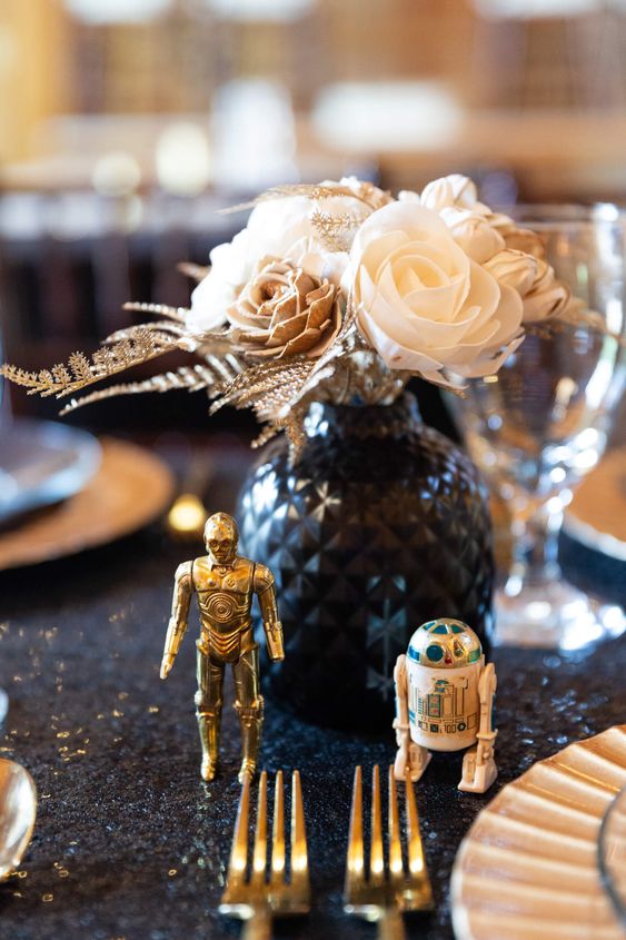 a chic Star Wars wedding centerpiece of a black vase with neutral blooms and figurines of droids for fun