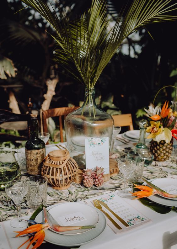 a chic tropical wedding tablescape with neutral linens, orange blooms and yellow ones, tropical elaves and tiny pineapples