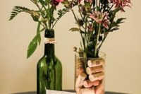 a cool vineyard wedding centerpiece of a wine bottle with blooms and a tall vase with corks and blooms plus candles