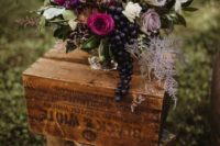 a fall vineyard wedding centerpiece of a silver vase, fuchsia, lilac and white blooms, greenery and grapes