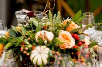 a fall vineyard wedding centerpiece of greenery, bright blooms, berries and mini pumpkins plus a wire table number
