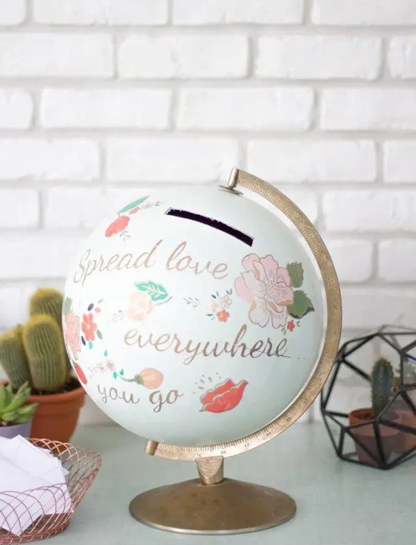 a globe with painted words and images and a gilded touches is a very cool wedding card box for a couple inspired by travelling