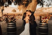a gorgeous vineyard fall wedding ceremony space with a living tree, barrels with bold floral arrangements, bold printed boho rugs
