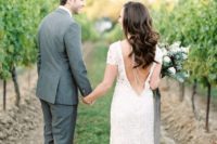 a lace sheath wedding dress with a cutout back, a layered back necklace and a train plus cap sleeves