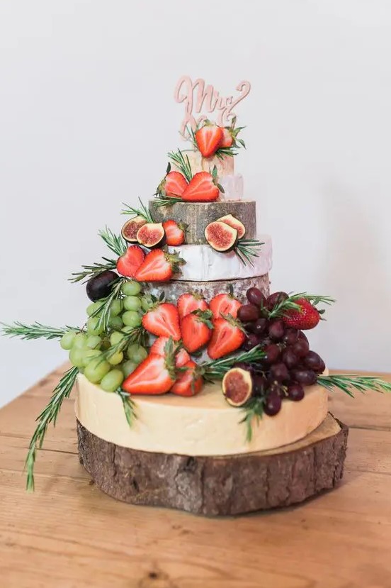 a lovely cheese wheel wedding cake decorated with grapes, strawberries and figs, herbs and a cake topper is a fantastic idea
