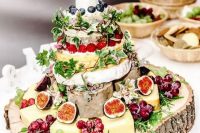 a messy cheese wheel and just cheese wedding tower with lots of fresh fruit and berries plus herbs is a gorgeous idea for a rustic wedding