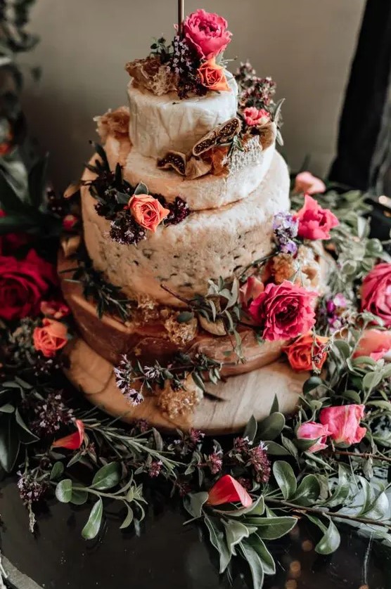 a messy cheese wheel wedding cake topped with orange and hot pink blooms plus herbs is a lovely idea for a boho summer wedding