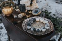 a moody sweets table with dried flowers, black candles, geodes and greenery plus a plate with macarons