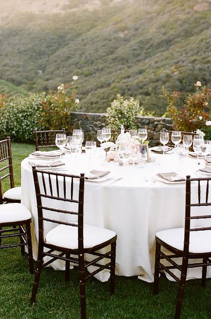 a neutral vineyard wedding reception with linens, grey menus and white chairs and a lovely vineyard view